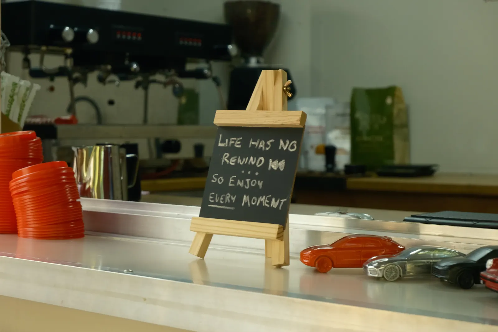 Espresso machine and grinder behind the Carmine counter, with a chalkboard and model cars in front