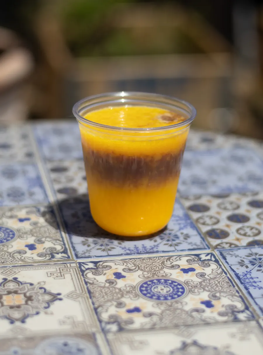 Iced drink with a layer of espresso over bright orange, on a tiled table