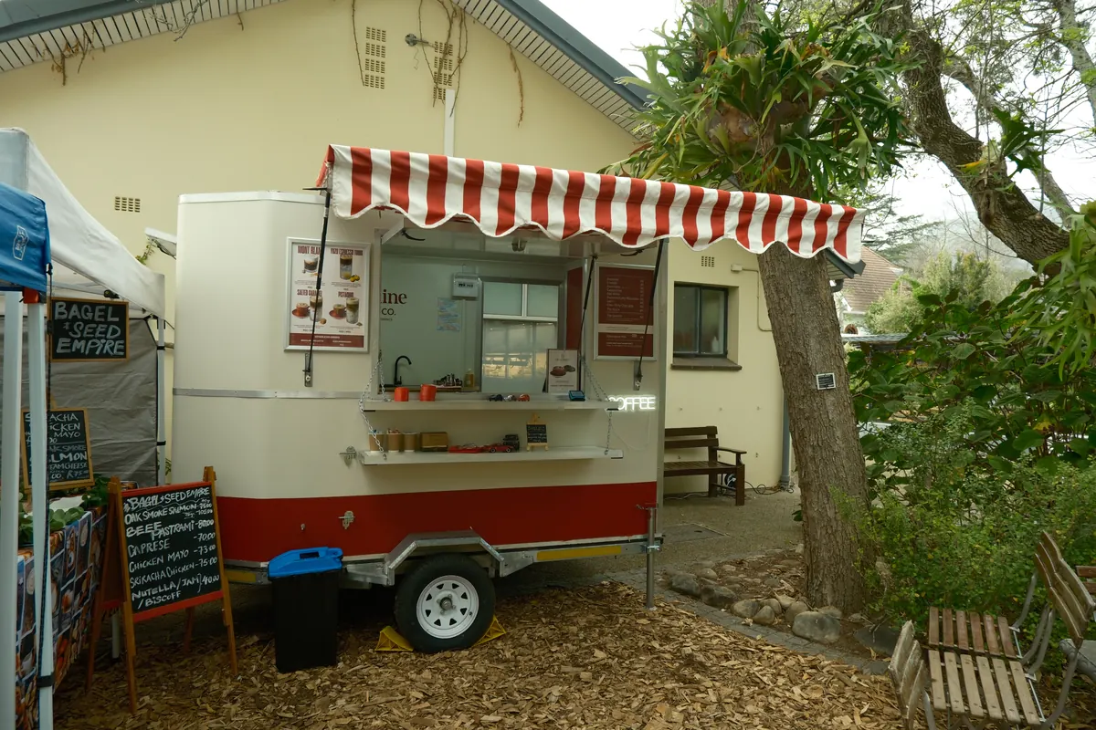 The Carmine trailer set up in a garden with a striped awning and café tables